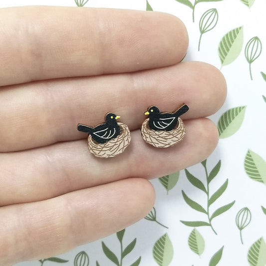 Wooden blackbird stud earrings held on hand, blackbird is sitting in nest and colours of black, brown and yellow