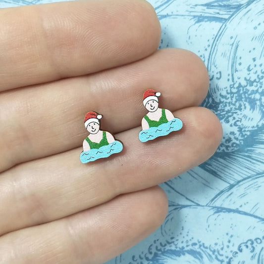 Christmas wild swimmer wooden stud earrings held on hand, the swimmers are wearing red santa hats