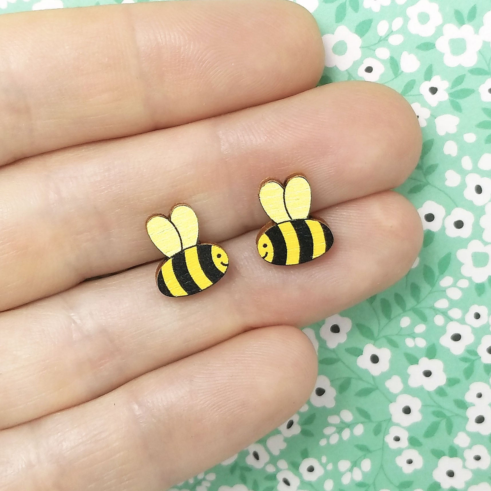 Wooden smiling bumble bee stud earrings held on hand, in yellow, gold and black
