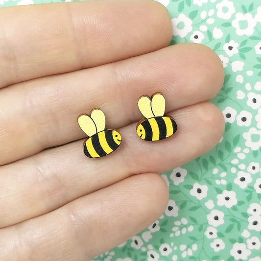 Wooden smiling bumble bee stud earrings held on hand, in yellow, gold and black