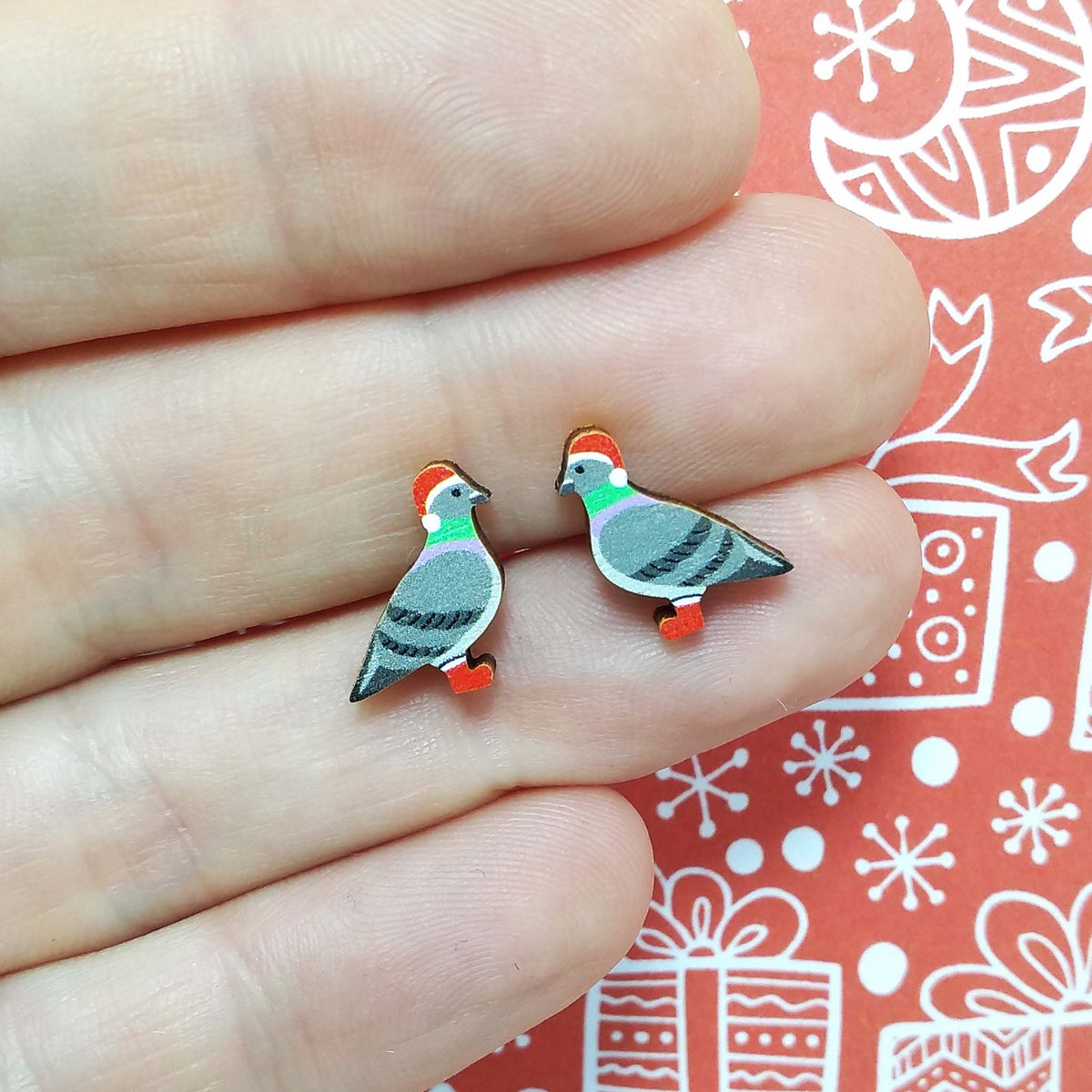 Christmas pigeon wooden stud earrings held on hand, the pigeons are wearing red santa hats and red boots