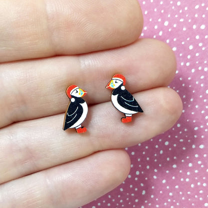 Christmas puffin wooden stud earrings held on hand, puffins are wearing red santa hats and red boots