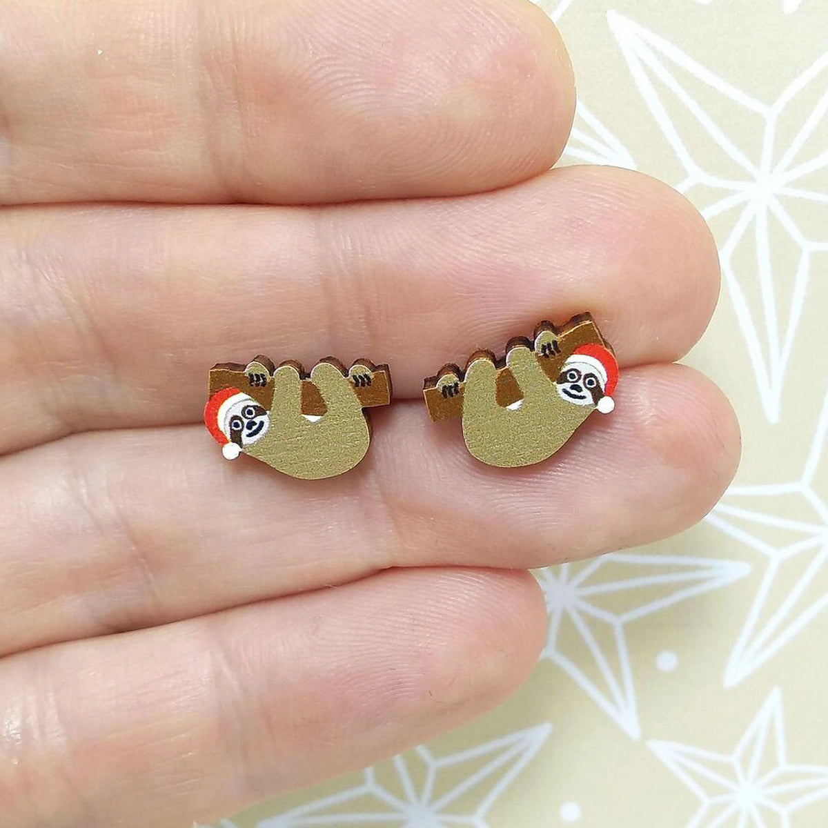Christmas sloth wooden stud earrings held on hand, the sloths are wearing red santa hats
