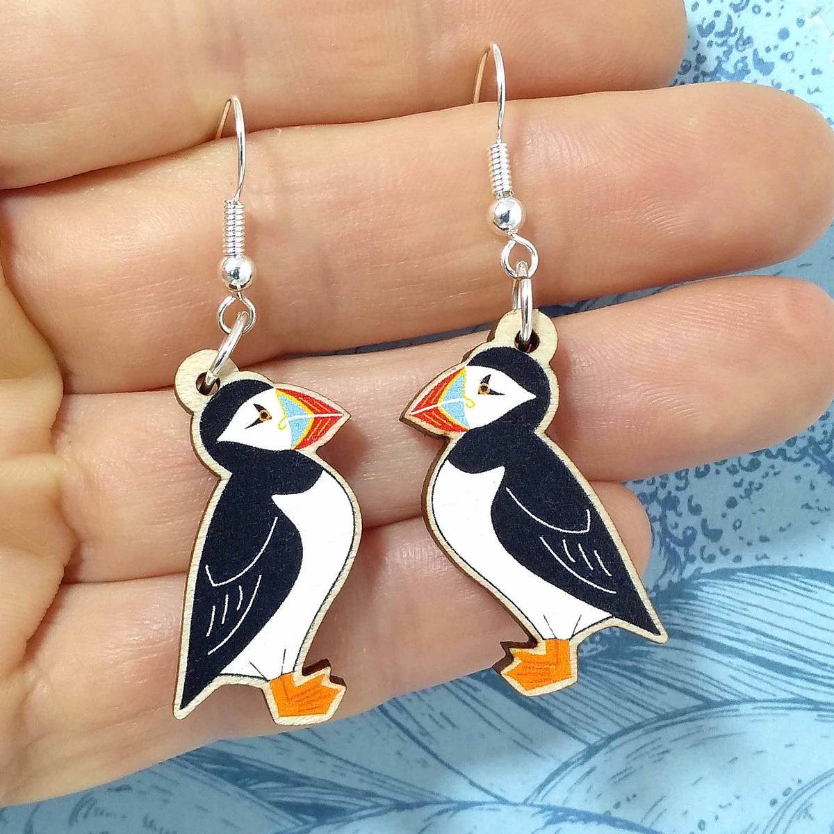 Wooden dangling puffin earrings held on hand