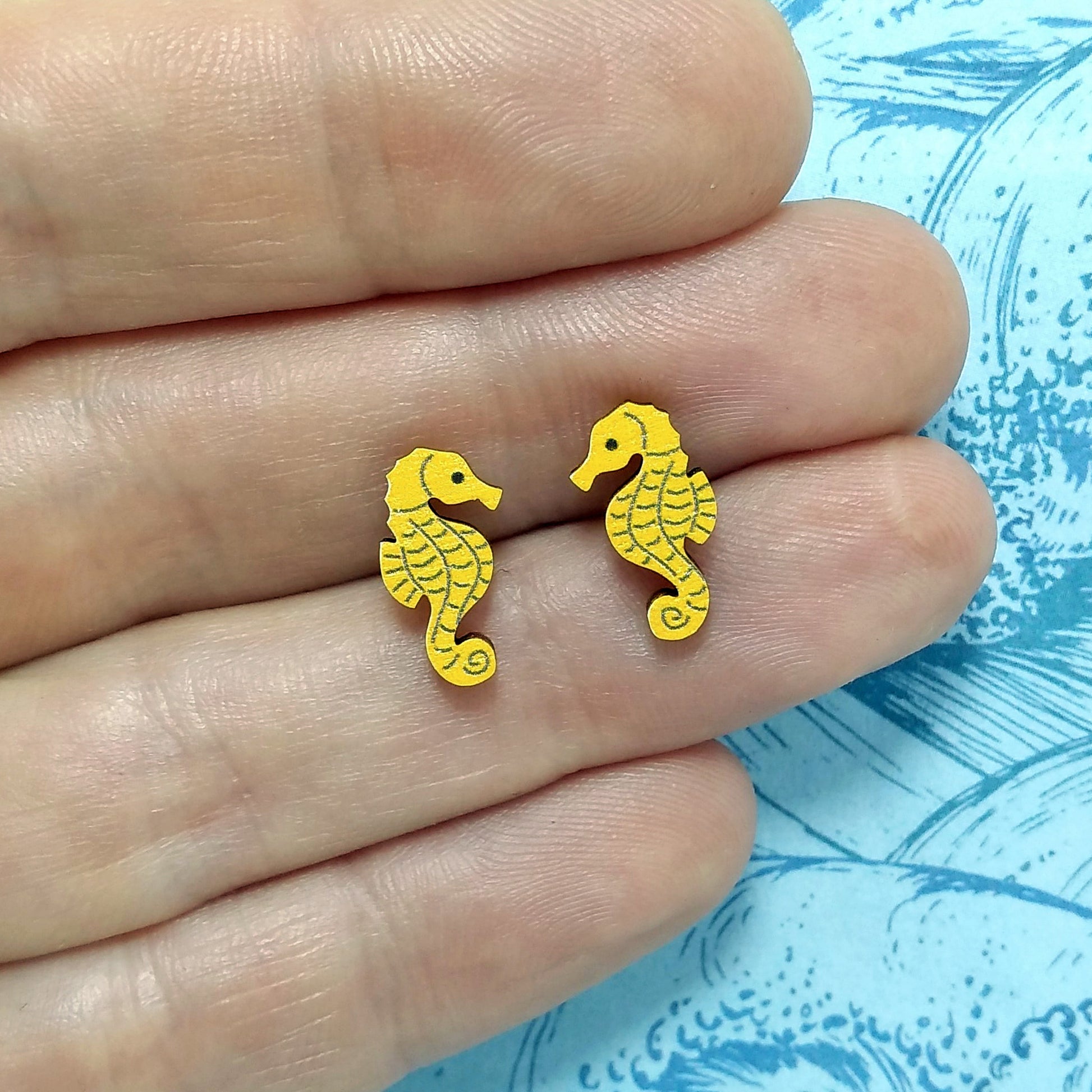 Wooden seahorse stud earrings held on hand