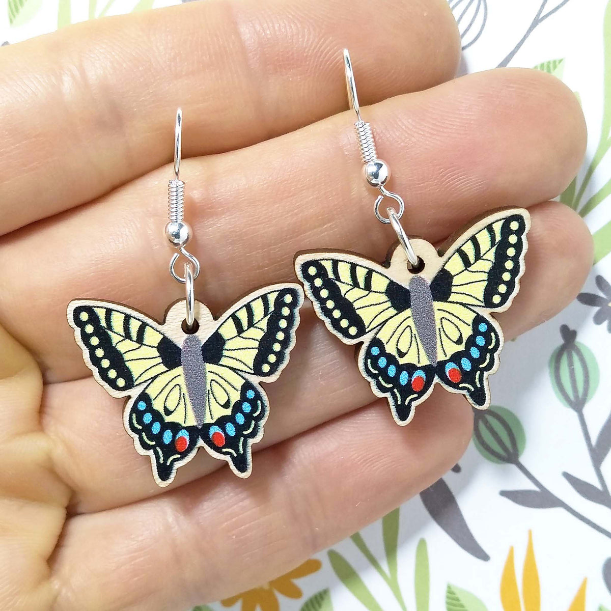 Wooden dangling swallowtail earrings held on hand